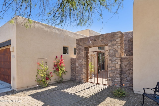 entrance to property featuring stone siding, a gate, stucco siding, and an attached garage