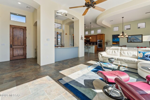 living room featuring ceiling fan with notable chandelier, arched walkways, a towering ceiling, and stone finish flooring