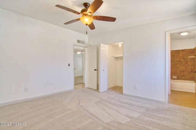 unfurnished bedroom with connected bathroom, a spacious closet, ceiling fan, carpet flooring, and visible vents