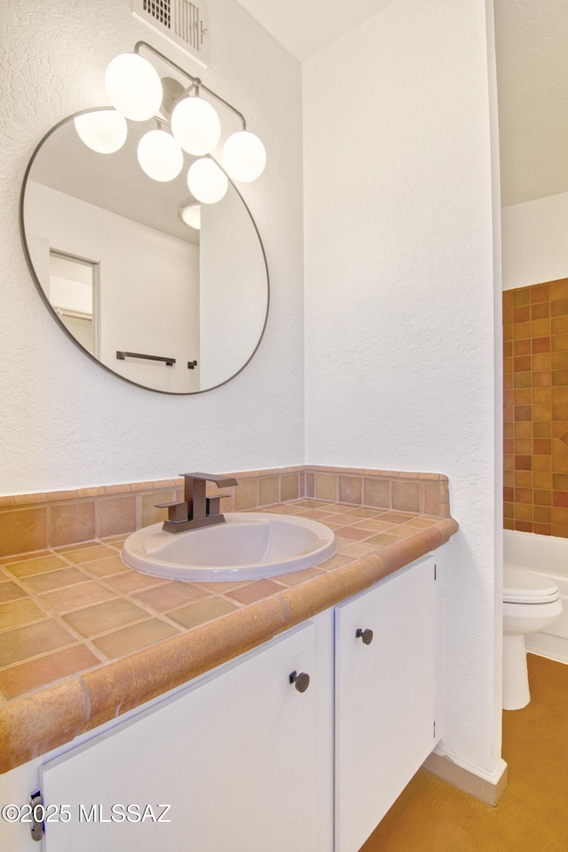 full bath with a textured wall, visible vents, toilet, and vanity