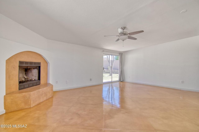 unfurnished living room with light tile patterned floors, baseboards, a fireplace with raised hearth, and ceiling fan