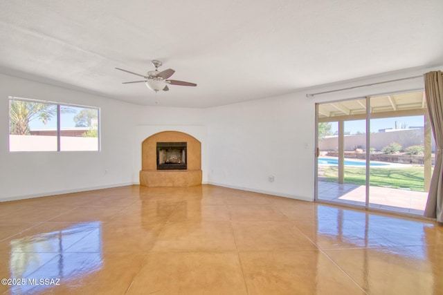 unfurnished living room featuring a fireplace with raised hearth, a ceiling fan, baseboards, and light tile patterned floors