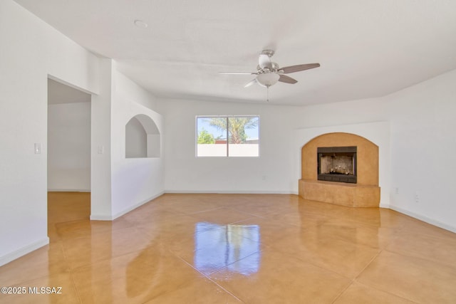 unfurnished living room featuring a ceiling fan, baseboards, and a fireplace with raised hearth