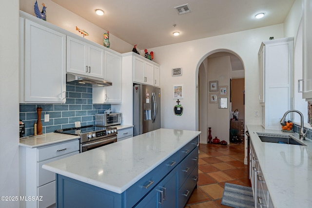 3437 S Abrego Dr, Green Valley, AZ 85614 - kitchen with blue cabinetry, under cabinet range hood, a sink, visible vents, and appliances with stainless steel finishes
