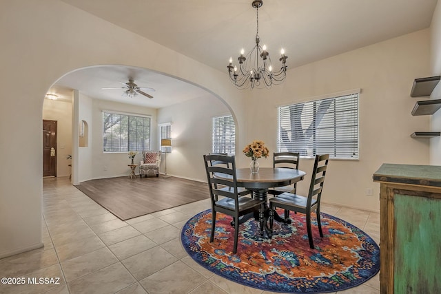 dining space featuring light tile patterned floors, arched walkways, baseboards, and ceiling fan with notable chandelier
