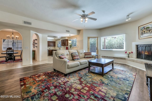 living room with arched walkways, ceiling fan with notable chandelier, light wood finished floors, and visible vents