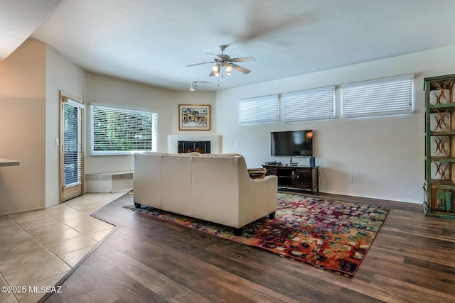 living room featuring baseboards, ceiling fan, light wood-type flooring, and a warm lit fireplace