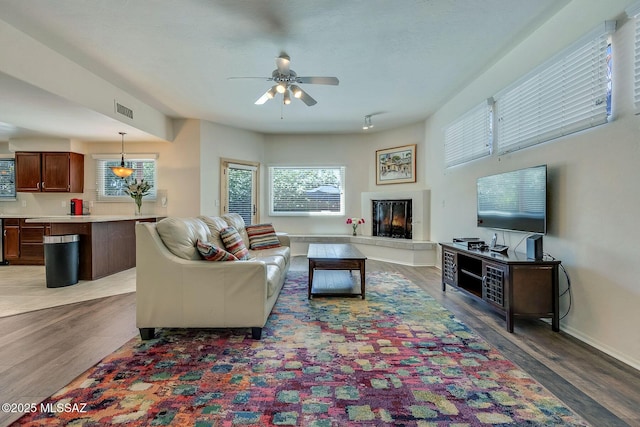 living room with visible vents, light wood-style flooring, ceiling fan, and a warm lit fireplace