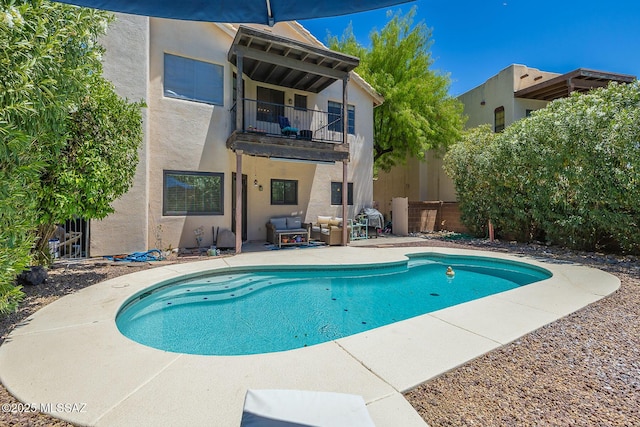 rear view of house with outdoor lounge area, a balcony, a patio, an outdoor pool, and stucco siding