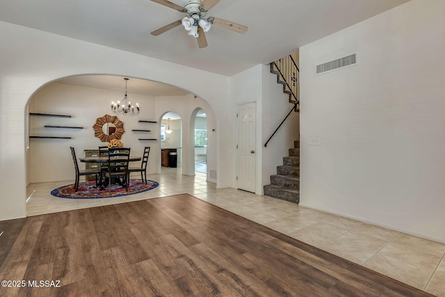 unfurnished dining area featuring arched walkways, ceiling fan with notable chandelier, stairs, wood finished floors, and visible vents