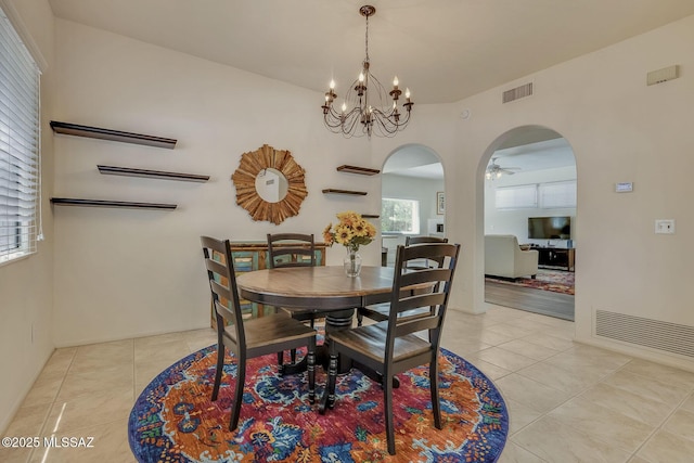 dining space with light tile patterned floors, arched walkways, ceiling fan with notable chandelier, and visible vents