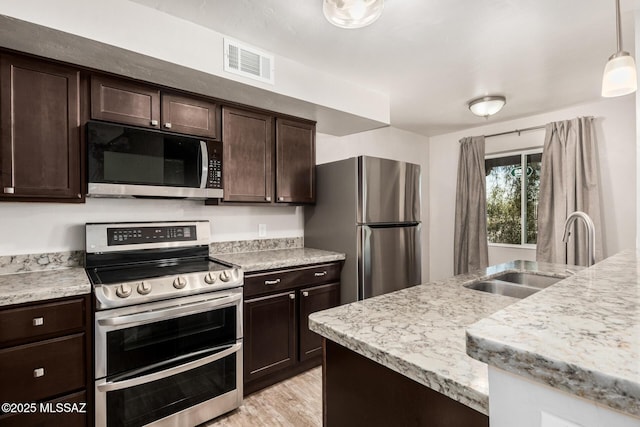 kitchen with dark brown cabinetry, visible vents, hanging light fixtures, a sink, and stainless steel appliances