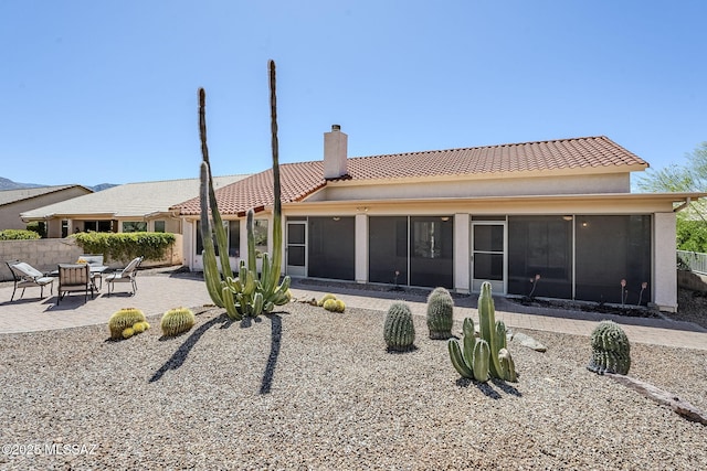 rear view of house with a tiled roof, a chimney, a sunroom, a patio, and stucco siding
