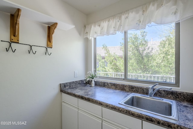kitchen featuring white cabinets, dark countertops, and a sink