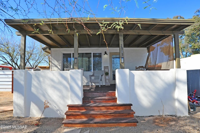 property entrance with stucco siding, fence, and a porch
