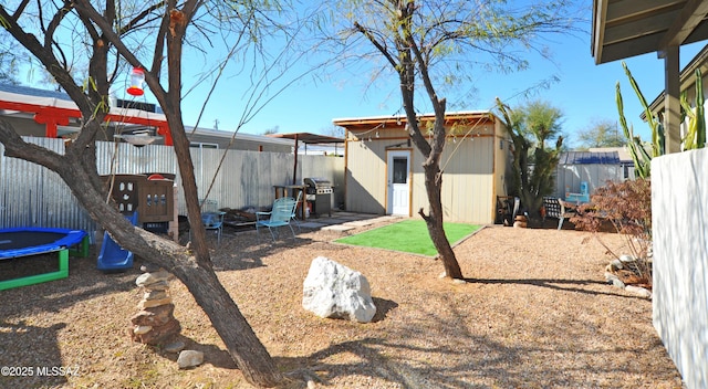 view of yard with a trampoline, a fenced backyard, an outbuilding, and a shed