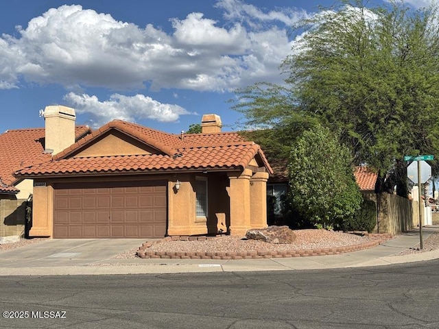 mediterranean / spanish home featuring a garage, stucco siding, a tiled roof, and a chimney