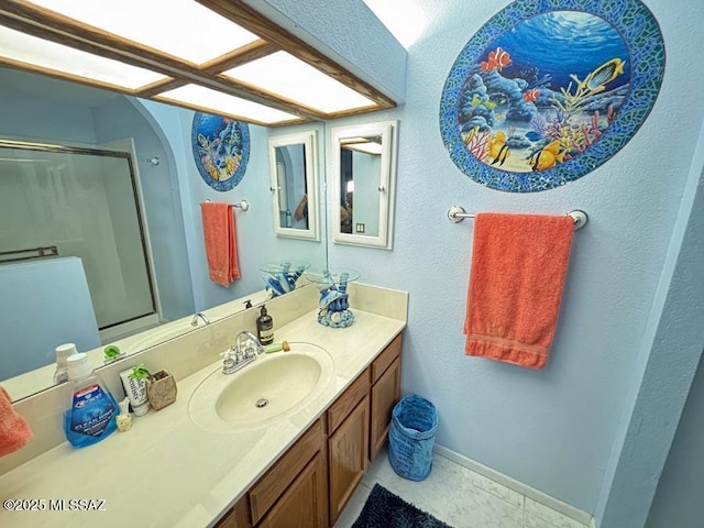 bathroom featuring a shower with door, baseboards, and vanity