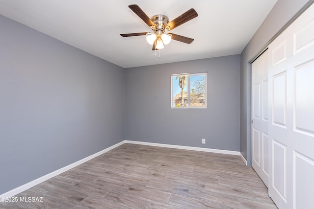 unfurnished bedroom featuring baseboards, wood finished floors, a closet, and a ceiling fan