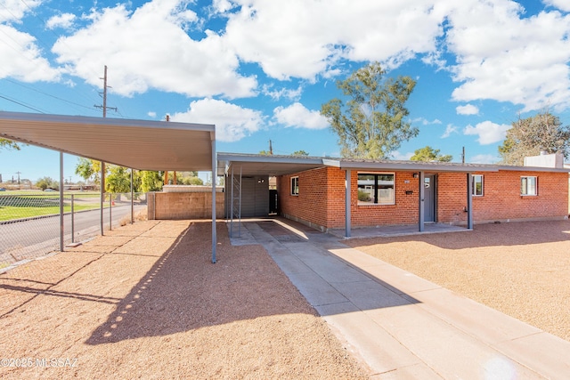 view of front of home featuring driveway, brick siding, fence, and a carport