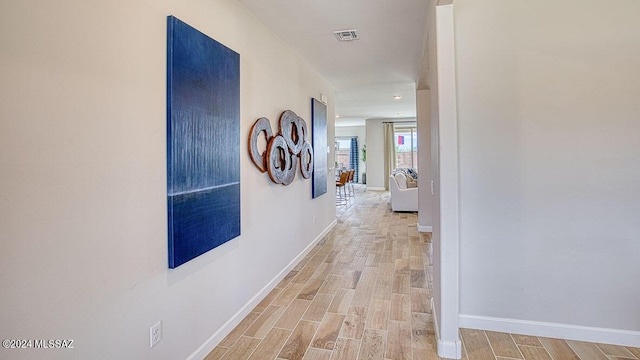 hallway with light wood-type flooring, baseboards, and visible vents