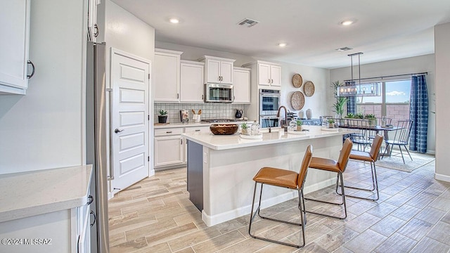 kitchen with a kitchen bar, stainless steel appliances, decorative backsplash, visible vents, and white cabinets