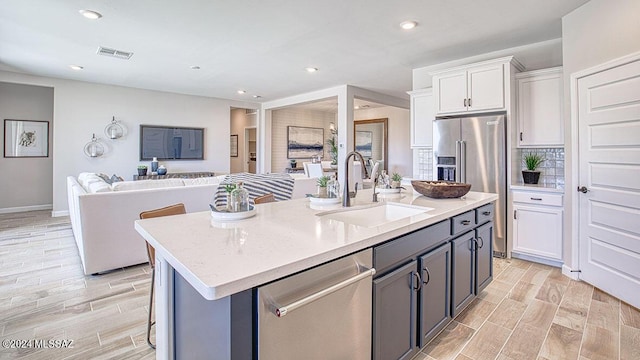 kitchen with a sink, stainless steel appliances, wood finish floors, visible vents, and white cabinets