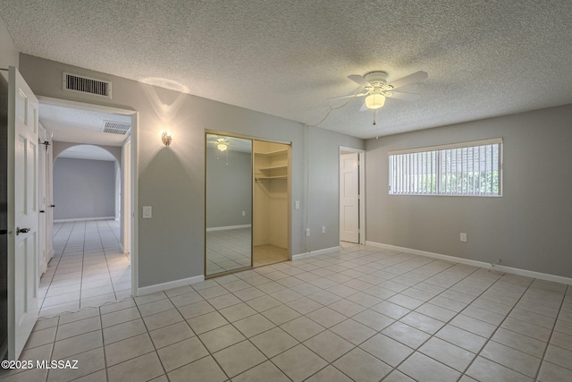 unfurnished bedroom featuring visible vents, a closet, arched walkways, and light tile patterned floors