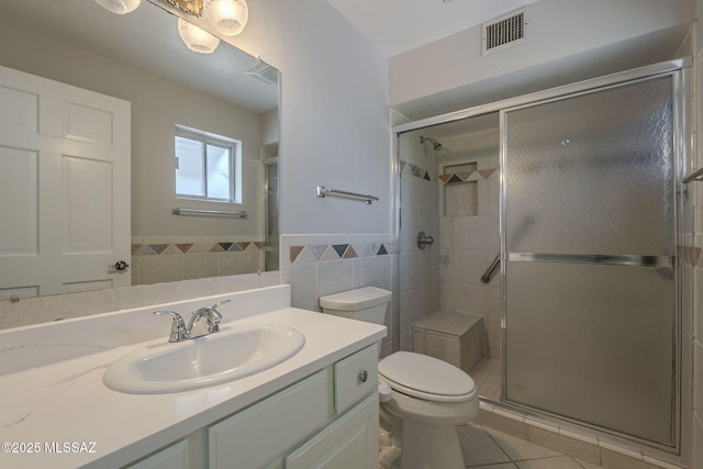 full bath with toilet, vanity, a shower stall, visible vents, and tile walls