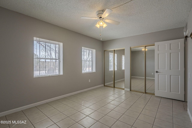 unfurnished bedroom with a textured ceiling, multiple closets, light tile patterned floors, baseboards, and ceiling fan