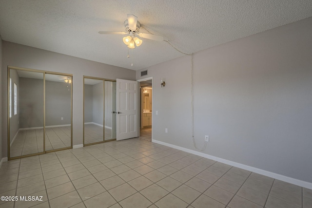 unfurnished bedroom featuring light tile patterned flooring, a textured ceiling, baseboards, visible vents, and two closets
