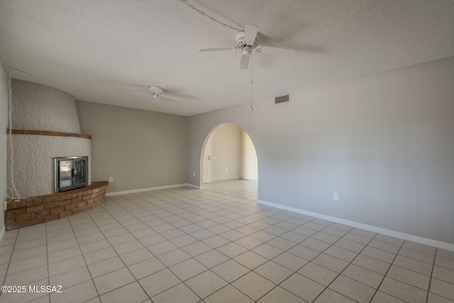 unfurnished living room featuring baseboards, arched walkways, ceiling fan, a brick fireplace, and visible vents