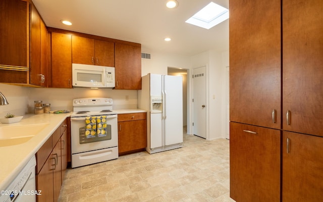 kitchen featuring white appliances, visible vents, brown cabinets, a skylight, and a sink
