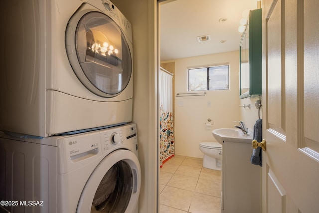 washroom featuring light tile patterned floors, stacked washer / dryer, visible vents, laundry area, and a sink
