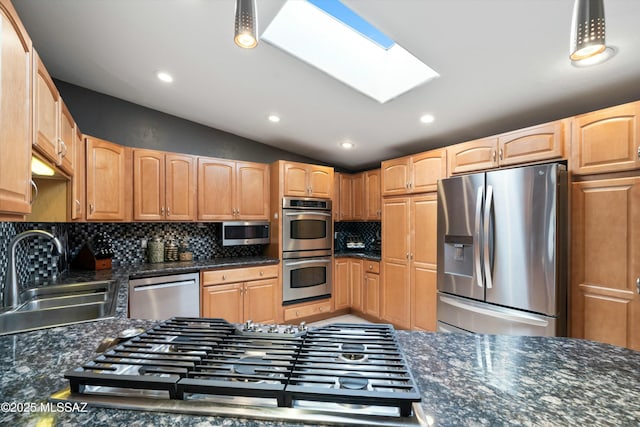 kitchen featuring lofted ceiling with skylight, stainless steel appliances, light brown cabinetry, backsplash, and a sink
