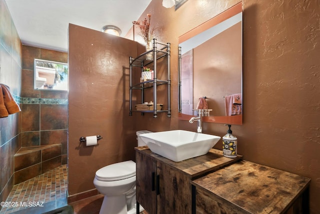 full bathroom featuring a textured wall, vanity, toilet, and walk in shower