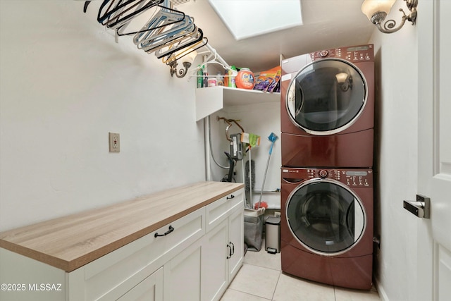 clothes washing area with a skylight, cabinet space, stacked washing maching and dryer, and light tile patterned floors