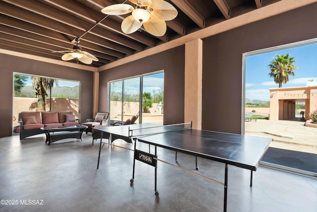 playroom featuring beamed ceiling, a ceiling fan, and finished concrete floors