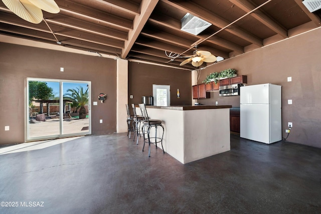 kitchen with stainless steel microwave, visible vents, concrete flooring, and freestanding refrigerator