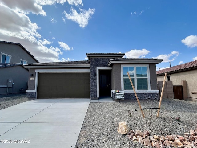 prairie-style home with stone siding, an attached garage, stucco siding, and driveway