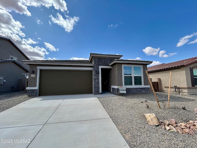 prairie-style house featuring stone siding, concrete driveway, stucco siding, and an attached garage