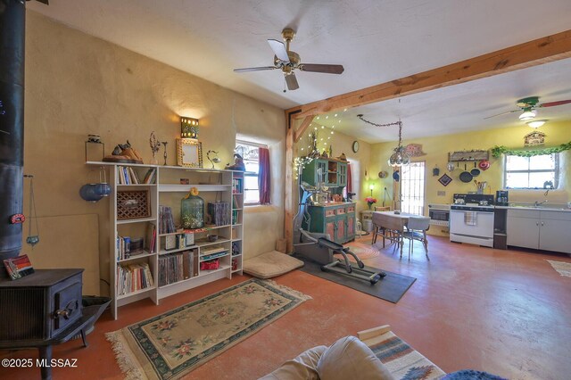 living room with beamed ceiling, a ceiling fan, and a wood stove