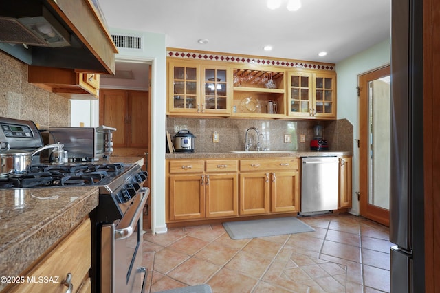 kitchen with a sink, tile counters, appliances with stainless steel finishes, custom range hood, and decorative backsplash