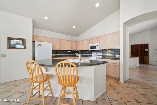 kitchen featuring light brown cabinetry, a sink, white appliances, and dark countertops
