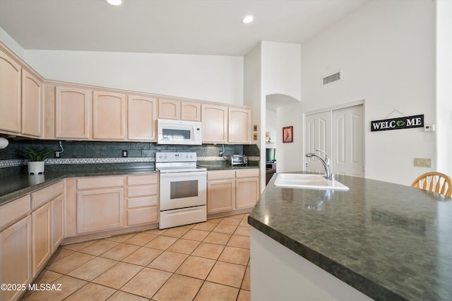 kitchen with a sink, light brown cabinetry, white appliances, and dark countertops