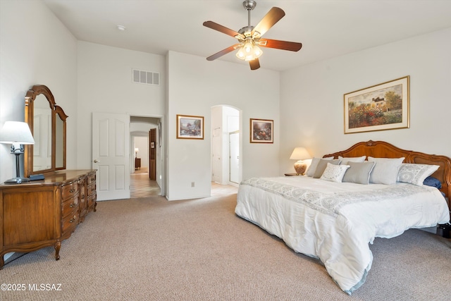 bedroom featuring visible vents, arched walkways, a high ceiling, a ceiling fan, and light colored carpet