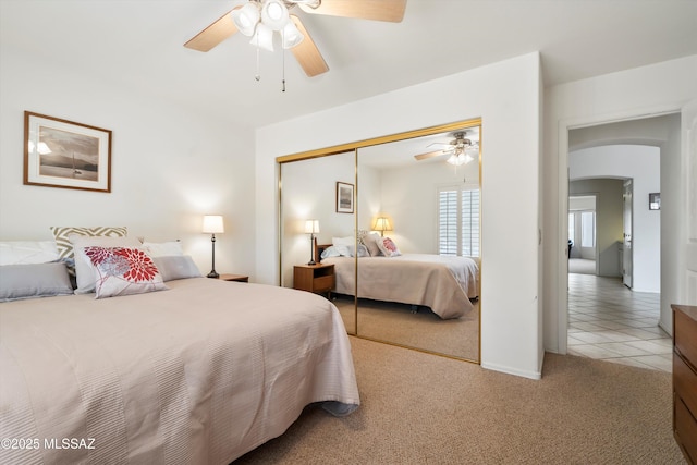 bedroom featuring arched walkways, a closet, a ceiling fan, tile patterned flooring, and carpet floors