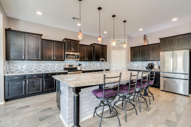 kitchen with a breakfast bar, backsplash, light stone countertops, visible vents, and stainless steel appliances