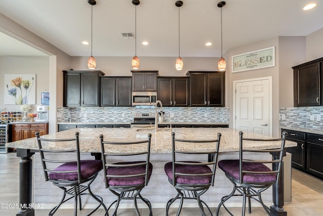 kitchen featuring light stone counters, a sink, appliances with stainless steel finishes, decorative backsplash, and a breakfast bar area