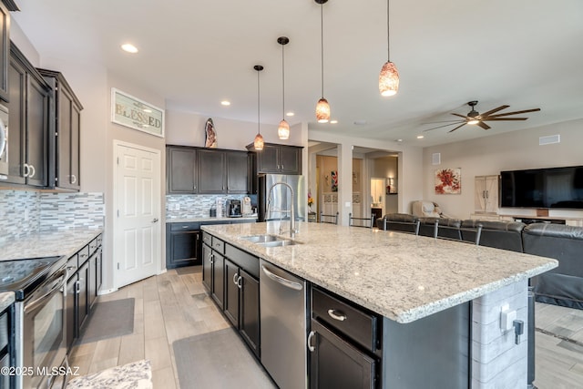 kitchen with tasteful backsplash, light stone counters, ceiling fan, stainless steel appliances, and a sink
